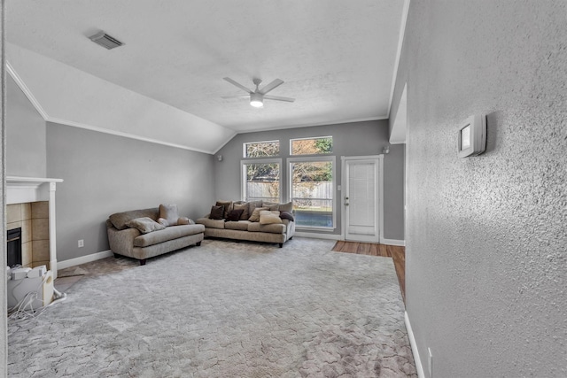 living room with vaulted ceiling, a textured ceiling, ornamental molding, ceiling fan, and a fireplace