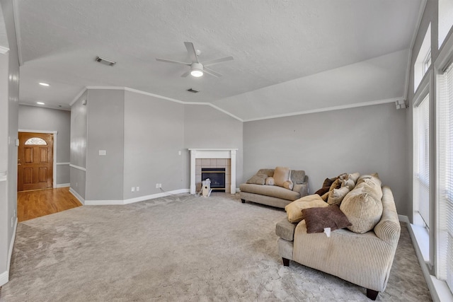 carpeted living room with ceiling fan, ornamental molding, a textured ceiling, a tiled fireplace, and vaulted ceiling