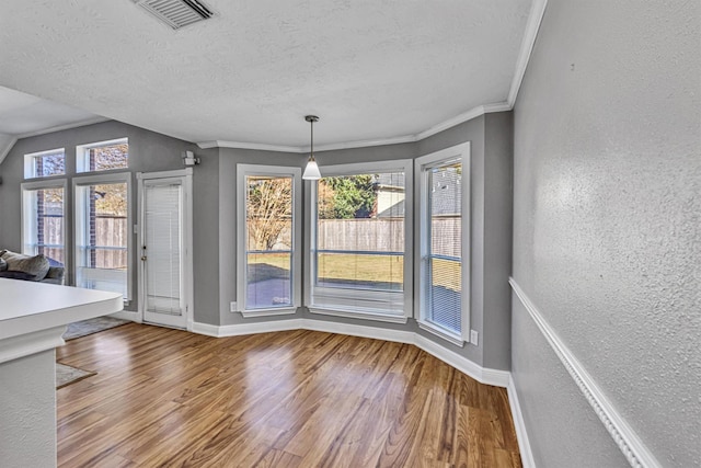 unfurnished dining area featuring hardwood / wood-style flooring, ornamental molding, and a textured ceiling