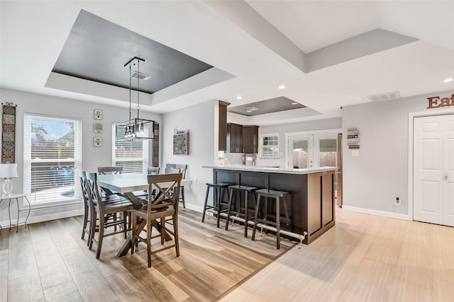 dining room featuring light wood-type flooring, a notable chandelier, and a tray ceiling