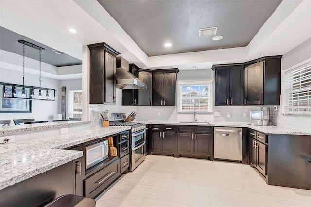 kitchen featuring pendant lighting, a raised ceiling, sink, appliances with stainless steel finishes, and light stone counters