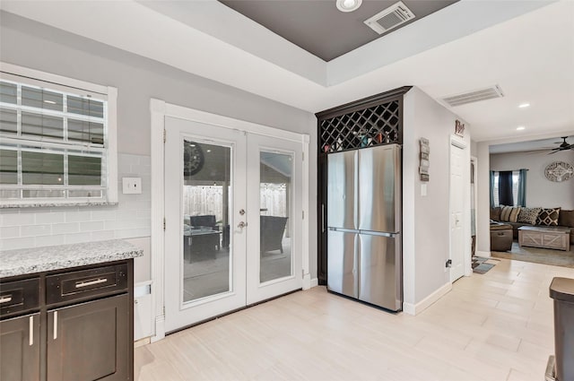 kitchen featuring ceiling fan, backsplash, stainless steel refrigerator, french doors, and light stone counters