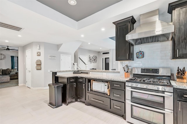 kitchen with tasteful backsplash, ceiling fan, double oven range, light stone countertops, and wall chimney exhaust hood