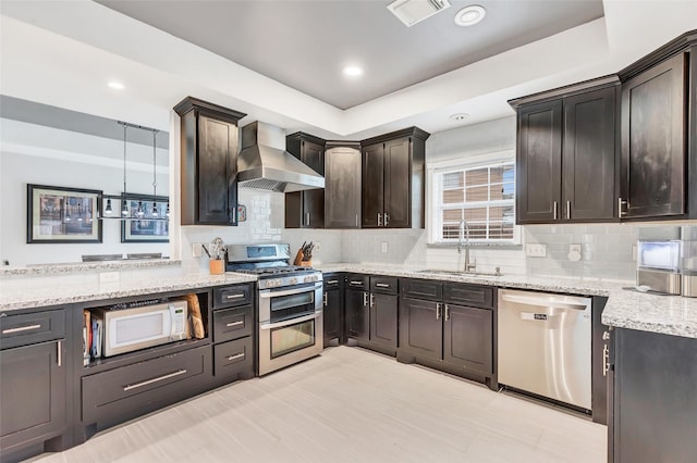 kitchen featuring tasteful backsplash, wall chimney range hood, sink, hanging light fixtures, and appliances with stainless steel finishes