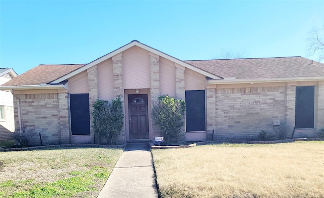 mid-century home featuring brick siding, a front lawn, and a shingled roof