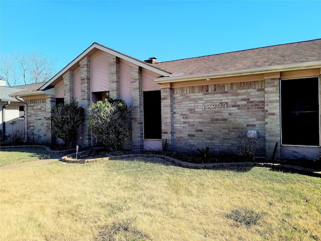 view of front of property featuring brick siding, a front yard, and a shingled roof