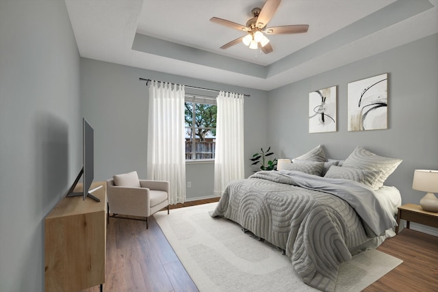 bedroom with ceiling fan, hardwood / wood-style floors, and a tray ceiling