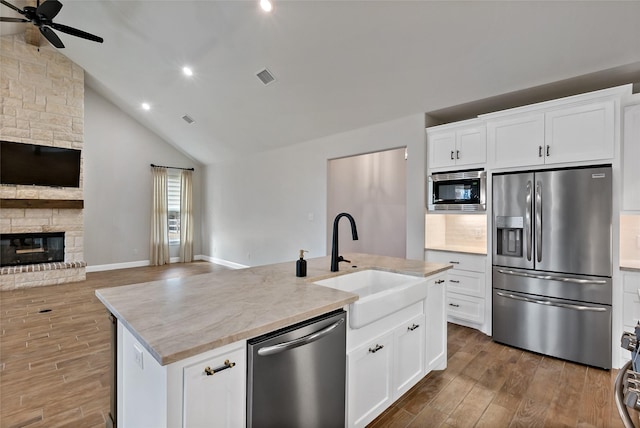 kitchen featuring white cabinetry, stainless steel appliances, a stone fireplace, sink, and a kitchen island with sink