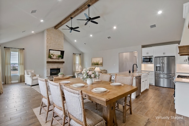 dining space featuring ceiling fan, beamed ceiling, a fireplace, high vaulted ceiling, and sink