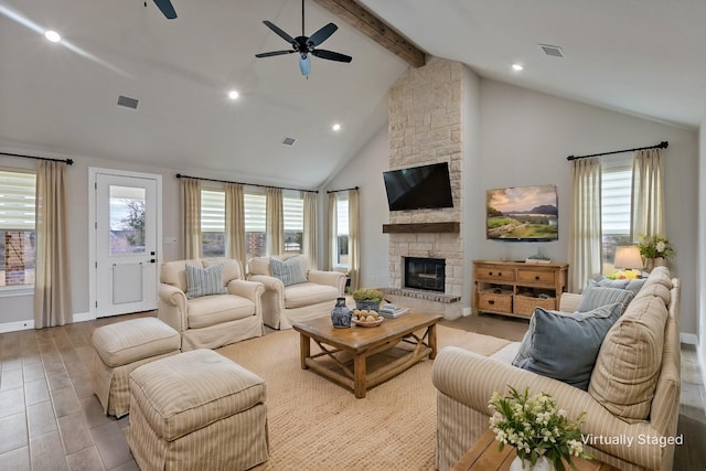 living room featuring ceiling fan, beam ceiling, a stone fireplace, and high vaulted ceiling