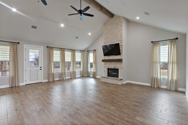 unfurnished living room featuring ceiling fan, beam ceiling, a stone fireplace, and a healthy amount of sunlight