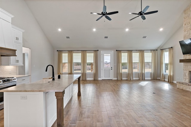 kitchen featuring white cabinetry, a stone fireplace, sink, gas range, and a center island with sink