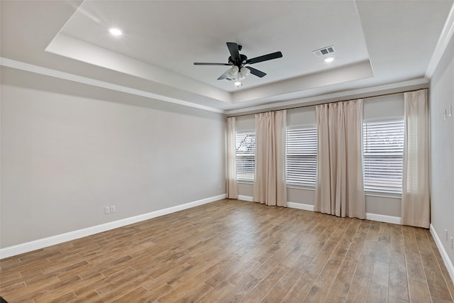 unfurnished room with light wood-type flooring, ceiling fan, a wealth of natural light, and a tray ceiling