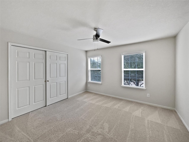 unfurnished bedroom with light carpet, a textured ceiling, a closet, and ceiling fan