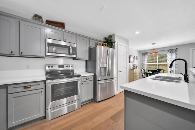 kitchen with stainless steel appliances, light hardwood / wood-style floors, sink, hanging light fixtures, and gray cabinetry