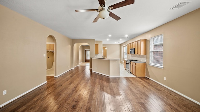 kitchen with ceiling fan, appliances with stainless steel finishes, backsplash, dark wood-type flooring, and a center island