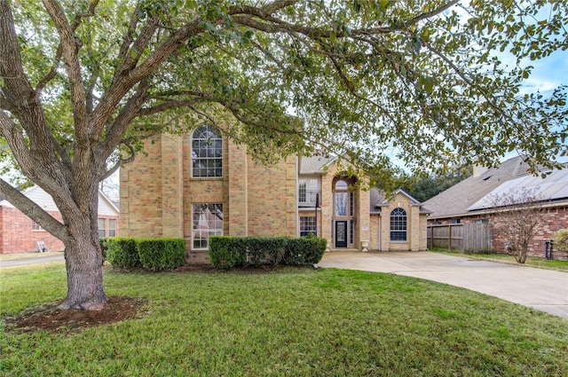 traditional-style home featuring a front yard, fence, and brick siding