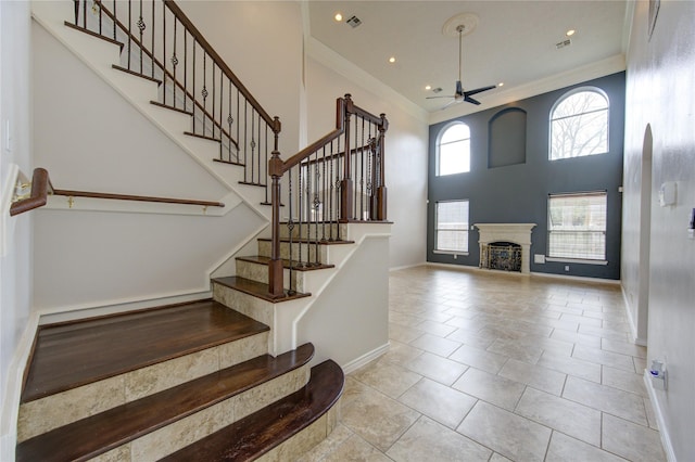 entryway featuring a towering ceiling, a fireplace, baseboards, and crown molding