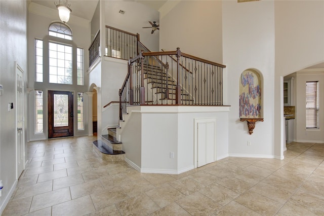 entryway with a ceiling fan, a towering ceiling, baseboards, and stairs