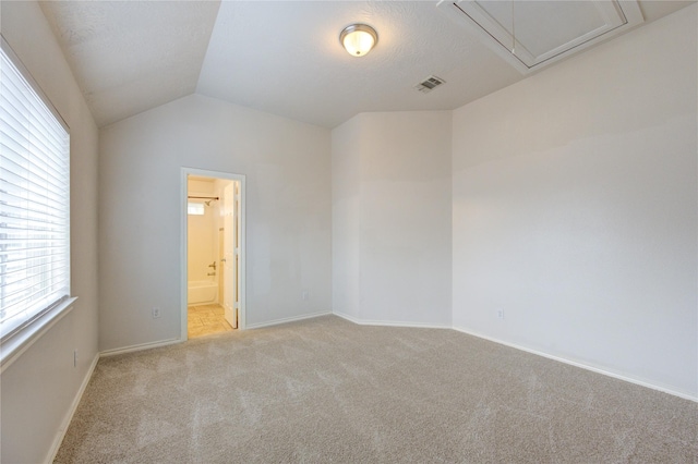 spare room with light colored carpet, visible vents, baseboards, vaulted ceiling, and attic access