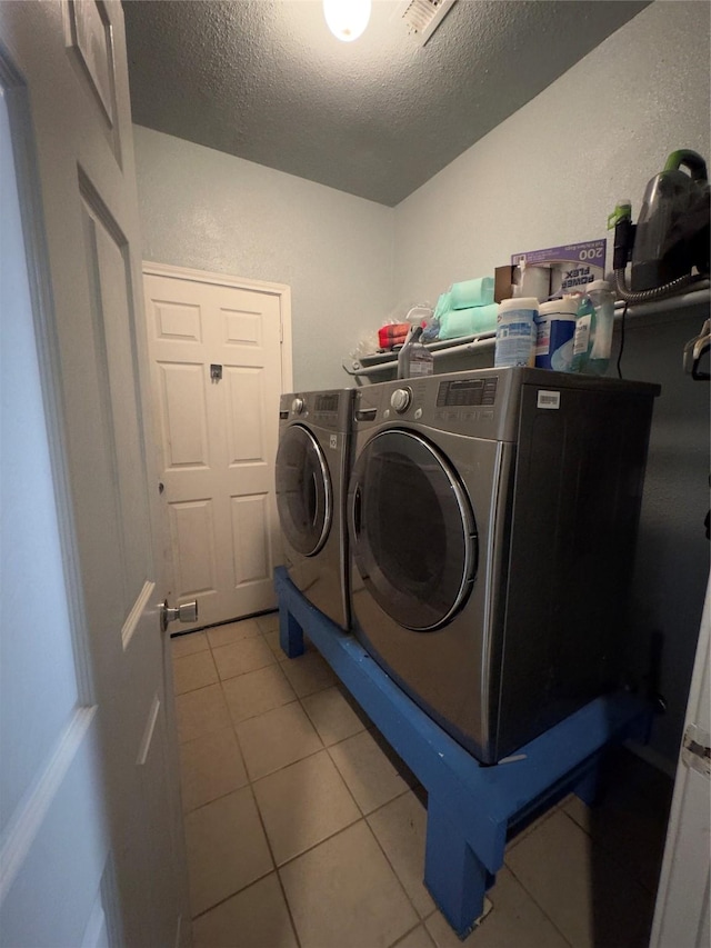 washroom featuring washer and clothes dryer, light tile patterned floors, and a textured ceiling