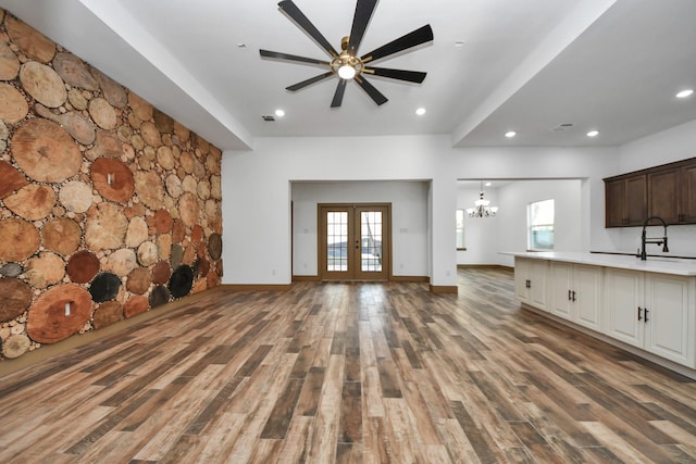 unfurnished living room featuring sink, ceiling fan with notable chandelier, dark wood-type flooring, and french doors