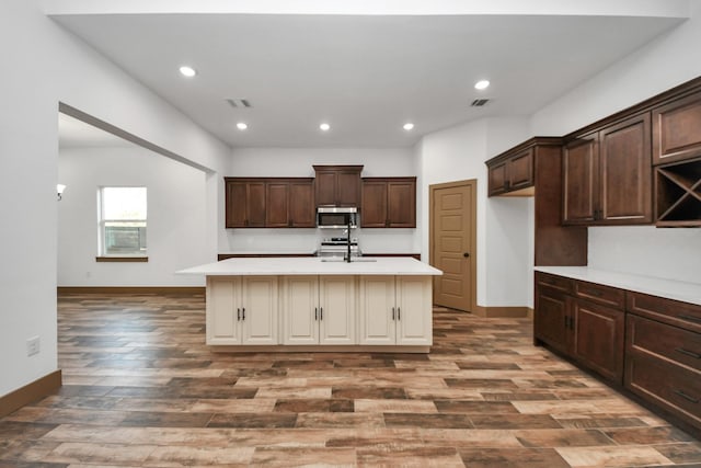 kitchen featuring dark wood-type flooring, dark brown cabinetry, sink, and an island with sink