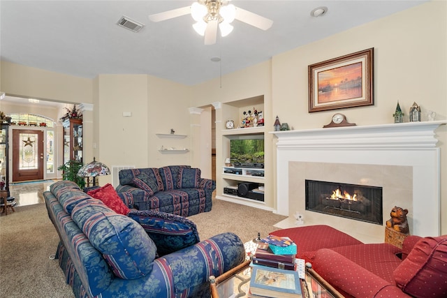 living room featuring a tile fireplace, carpet floors, ceiling fan, and built in shelves