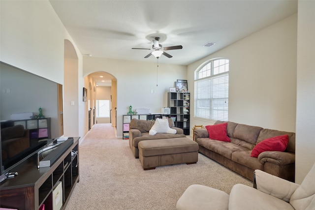 carpeted living room with visible vents, arched walkways, and a ceiling fan