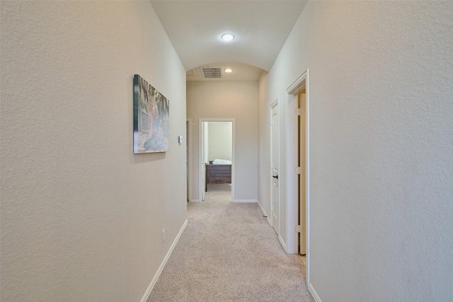 hall featuring visible vents, lofted ceiling, arched walkways, baseboards, and light colored carpet