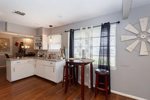 kitchen featuring kitchen peninsula, light stone countertops, sink, white cabinets, and pendant lighting