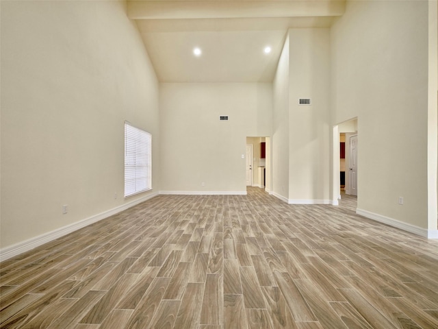 spare room with beam ceiling, a high ceiling, and light hardwood / wood-style flooring