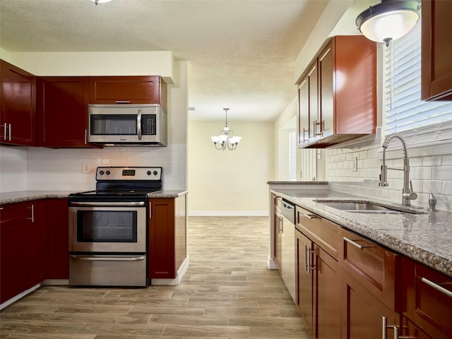 kitchen with pendant lighting, sink, an inviting chandelier, stainless steel appliances, and light stone counters