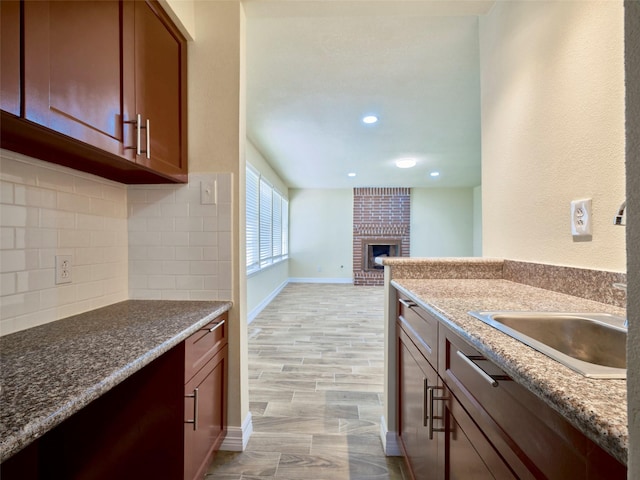 kitchen featuring light hardwood / wood-style floors, a brick fireplace, decorative backsplash, stone counters, and sink