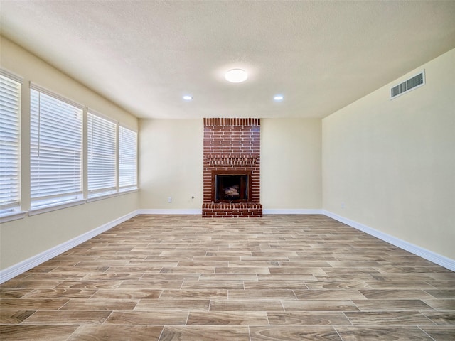 unfurnished living room with a textured ceiling, light hardwood / wood-style flooring, and a fireplace