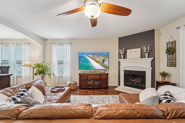 living room with ceiling fan, wood-type flooring, and a large fireplace