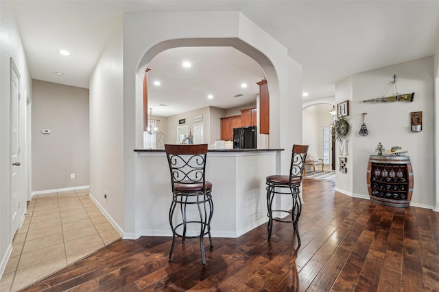 kitchen featuring hardwood / wood-style floors, kitchen peninsula, an inviting chandelier, a kitchen breakfast bar, and black refrigerator