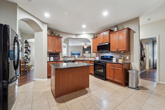 kitchen featuring light tile patterned floors, dark stone counters, a kitchen island, black appliances, and sink