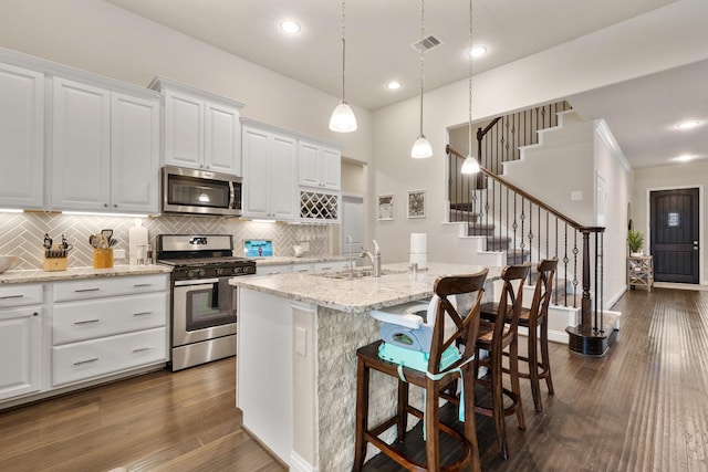 kitchen with pendant lighting, white cabinets, appliances with stainless steel finishes, sink, and a center island with sink