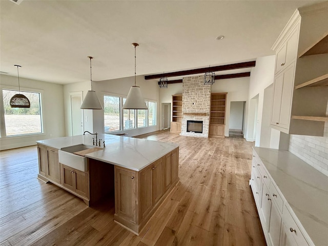 kitchen featuring sink, a large island with sink, a healthy amount of sunlight, and a fireplace