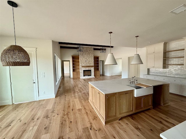 kitchen with a large island with sink, decorative light fixtures, a stone fireplace, sink, and backsplash