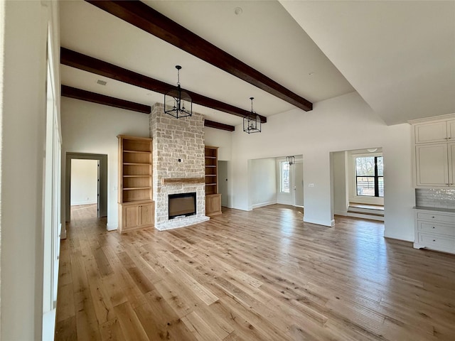 unfurnished living room featuring an inviting chandelier, beam ceiling, light hardwood / wood-style flooring, and a stone fireplace