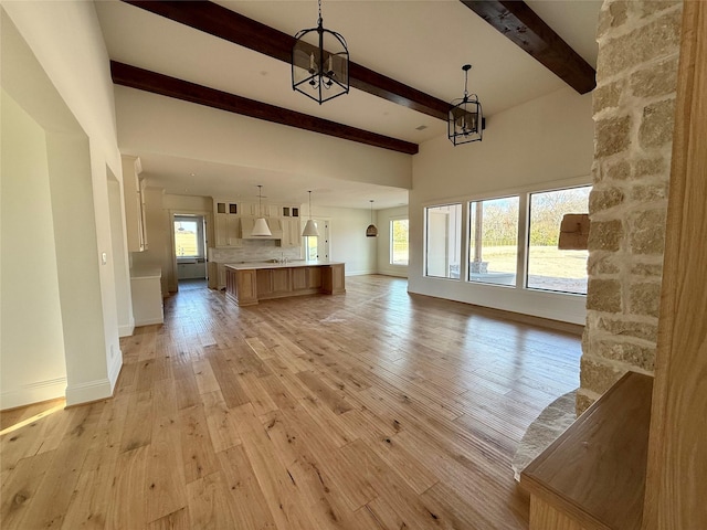 unfurnished living room featuring beam ceiling, a chandelier, and light wood-type flooring