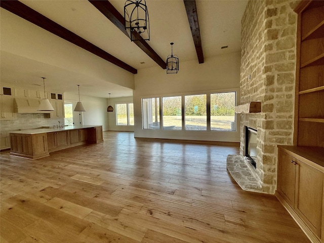 unfurnished living room featuring beam ceiling, an inviting chandelier, a wealth of natural light, and a stone fireplace