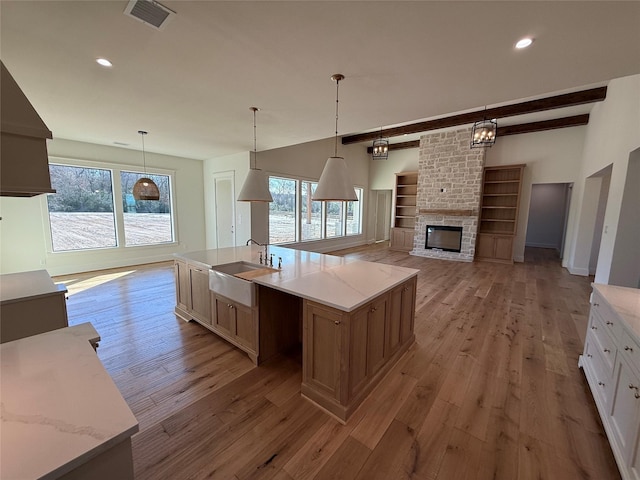 kitchen with sink, white cabinetry, light stone counters, hanging light fixtures, and a kitchen island with sink