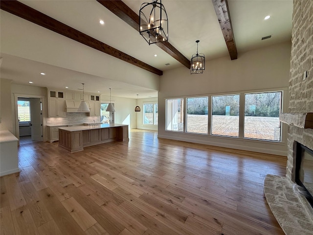 unfurnished living room featuring beamed ceiling, light wood-type flooring, a notable chandelier, and a fireplace