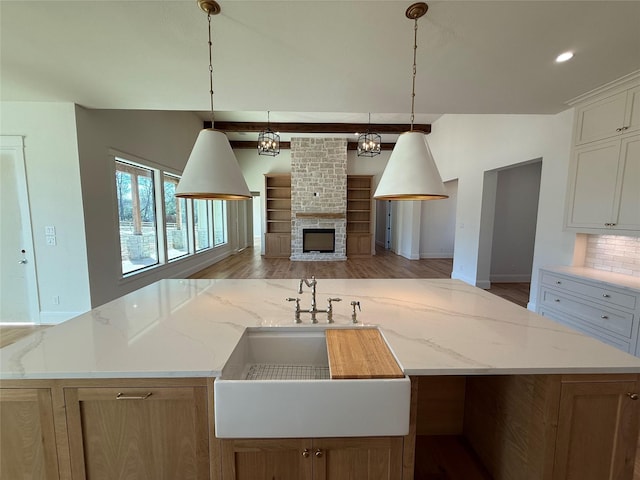 kitchen featuring sink, light stone countertops, white cabinets, a center island with sink, and decorative light fixtures