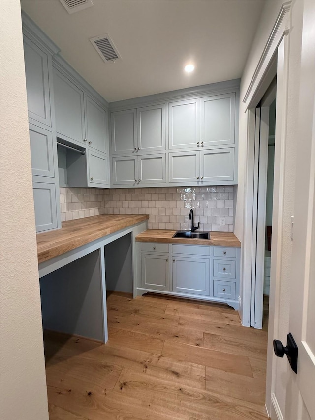 kitchen with tasteful backsplash, sink, wood counters, and light hardwood / wood-style flooring