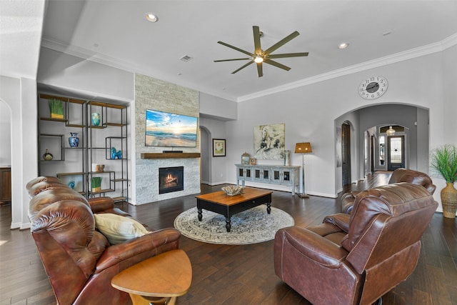 living room with dark wood-type flooring, ceiling fan, ornamental molding, and a fireplace