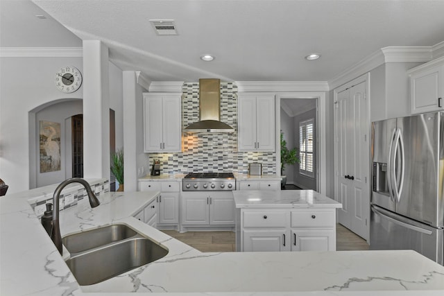 kitchen with sink, appliances with stainless steel finishes, white cabinetry, light stone counters, and wall chimney exhaust hood